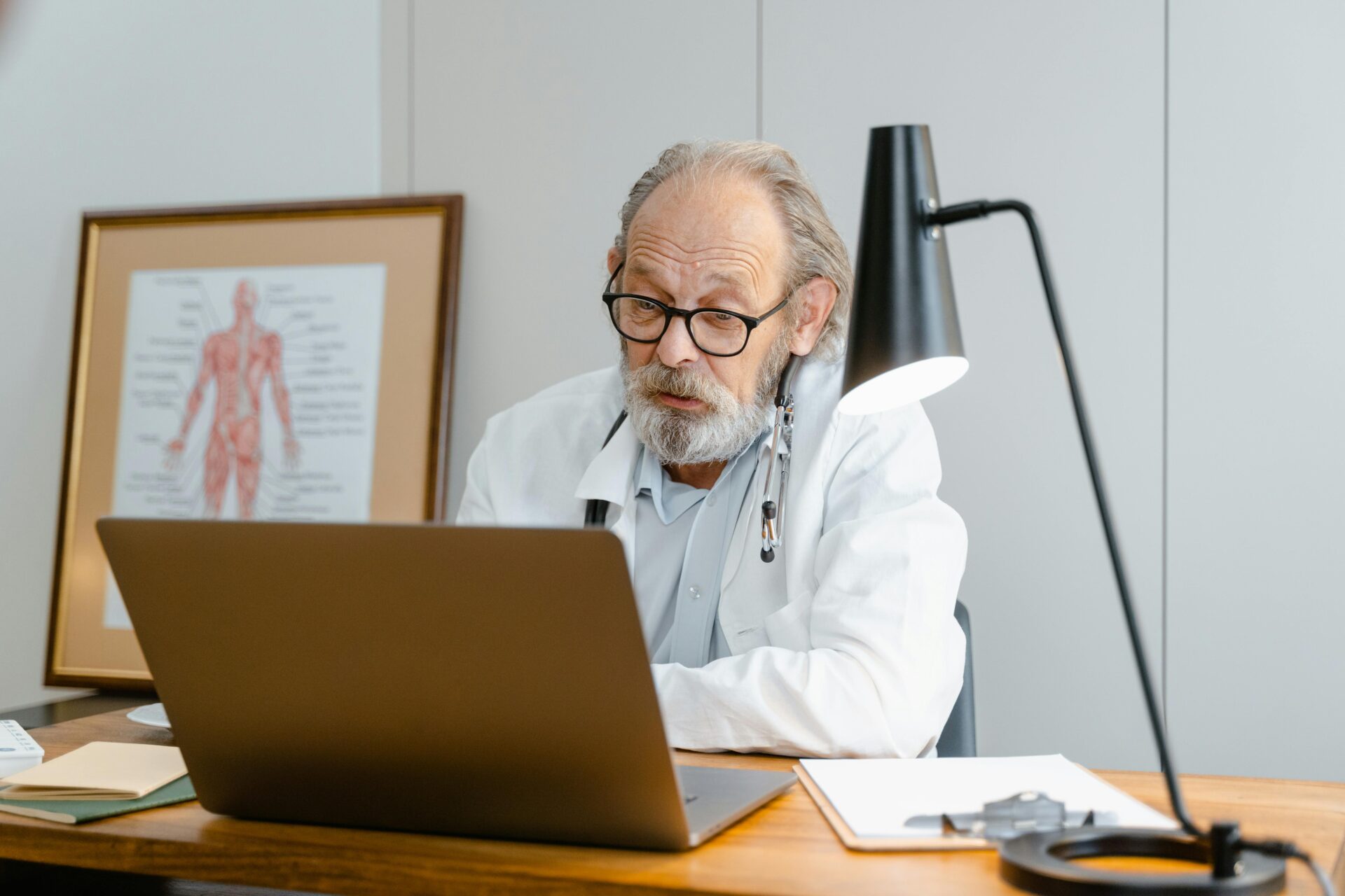 A doctor sitting at a table, looking into a laptop